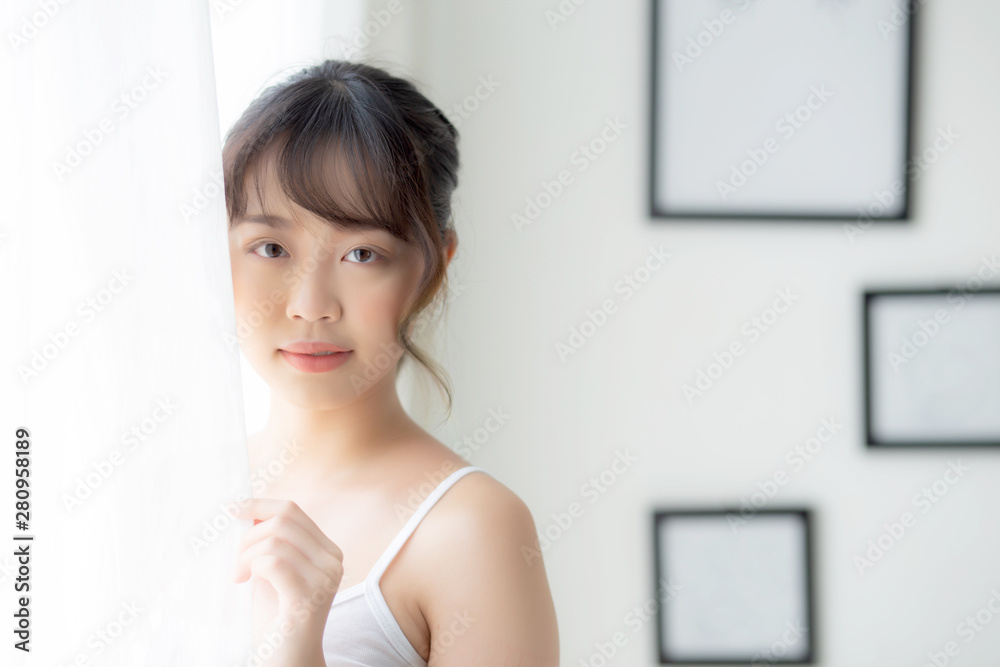 Portrait of beautiful young asian woman standing at the window and smile while wake up with sunlight at morning, girl happy with fresh and cheerful, lifestyle and relax for wellness concept. Portrait of beautiful young asian woman standing at the window and smile while wake up with sunlight at morning, girl happy with fresh and cheerful, lifestyle and relax for wellness concept.