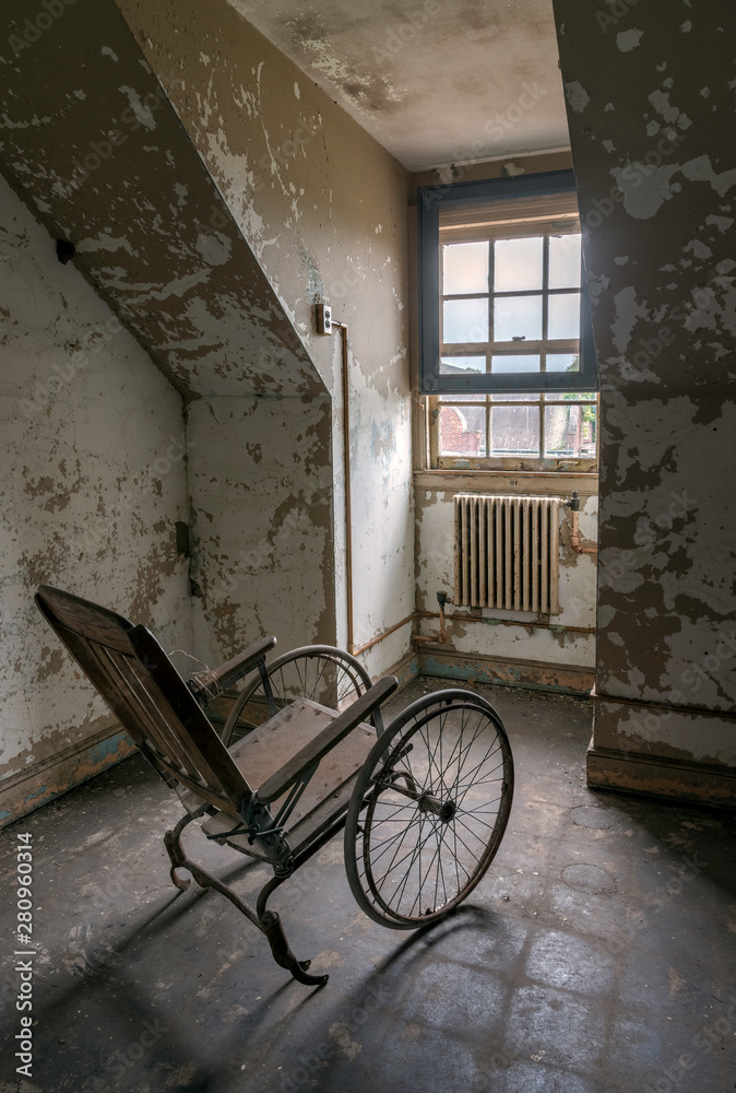 Empty wheelchair facing a window in an abandoned asylum