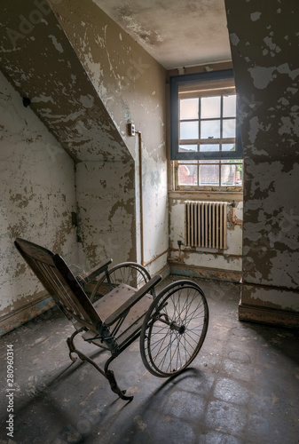 Empty wheelchair facing a window in an abandoned asylum