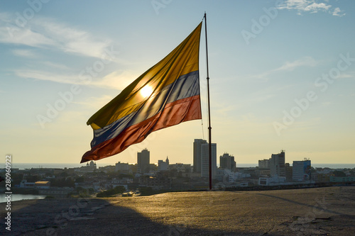 Warm Sunset behind Colombian flag in Castillo San Felipes de Barajas with the landscape view of the Cartagena`s city in the background (Cartagena - Colombia) photo