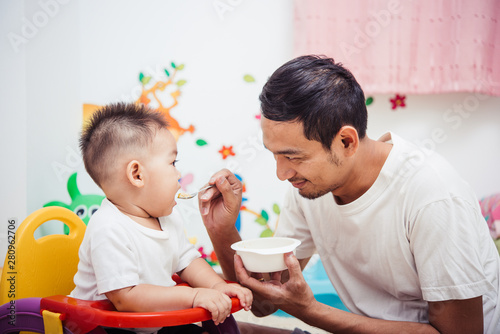 Father acting Mom feeding his son baby 1 year old on chair