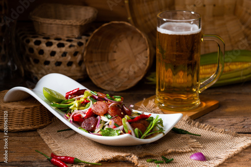 Spicy Chinese pork sausage with vegetable Thai salad in white plate on wood background