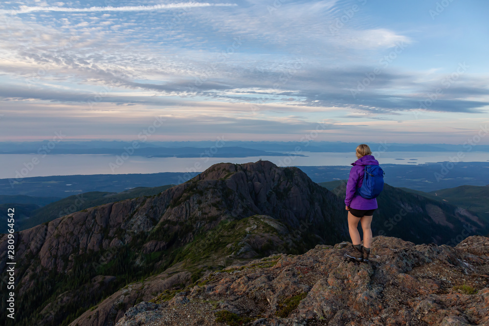 Fototapeta premium Adventurous girl hiking the beautiful trail in the Canadian Mountain Landscape during a vibrant summer sunset. Taken at Mt Arrowsmith, near Nanaimo, Vancouver Island, BC, Canada.