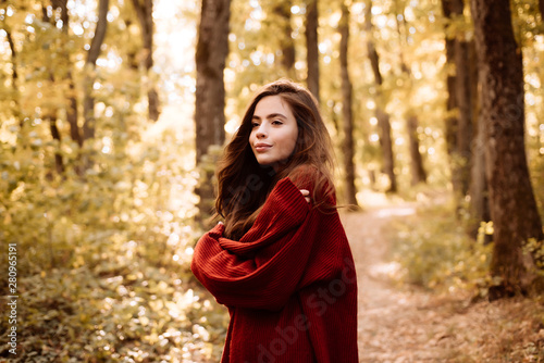Carefree young woman in trendy vintage red pullover or sweater. Pretty woman walking in the Park and enjoying the beautiful autumn nature.