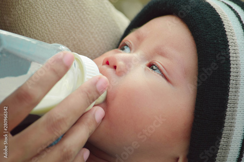 closeup portrait of beautifull baby boy drinking milk from his mother from feeding bottle