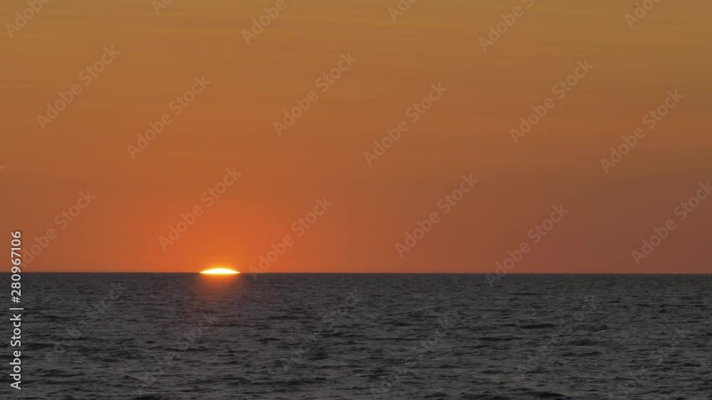 Romantic sunset over the calm Baltic sea, big red Sun sets over the horizon in summer, medium shot from a distance Romantic sunset over the calm Baltic sea, big red Sun sets over the horizon in summer, medium shot from a distance