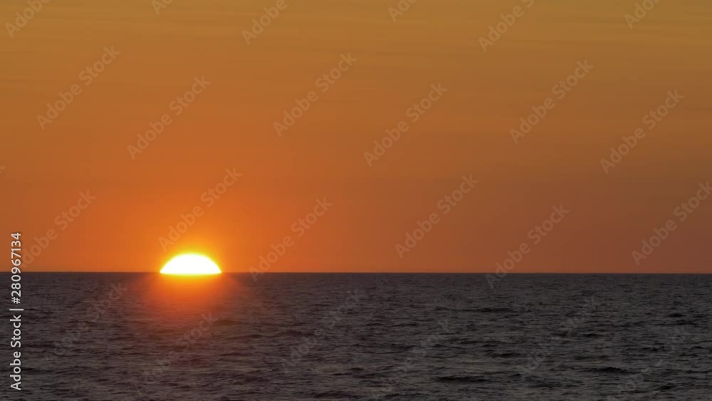 Romantic sunset over the calm Baltic sea, big red Sun sets over the horizon in summer, medium shot from a distance Romantic sunset over the calm Baltic sea, big red Sun sets over the horizon in summer, medium shot from a distance
