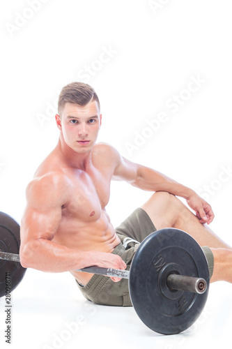 Muscular man working out in studio doing exercises with barbell at biceps, strong male naked torso abs. Isolated on white background. Copy Space. Rest, Sits on the floor at the barbell. Fatigue.