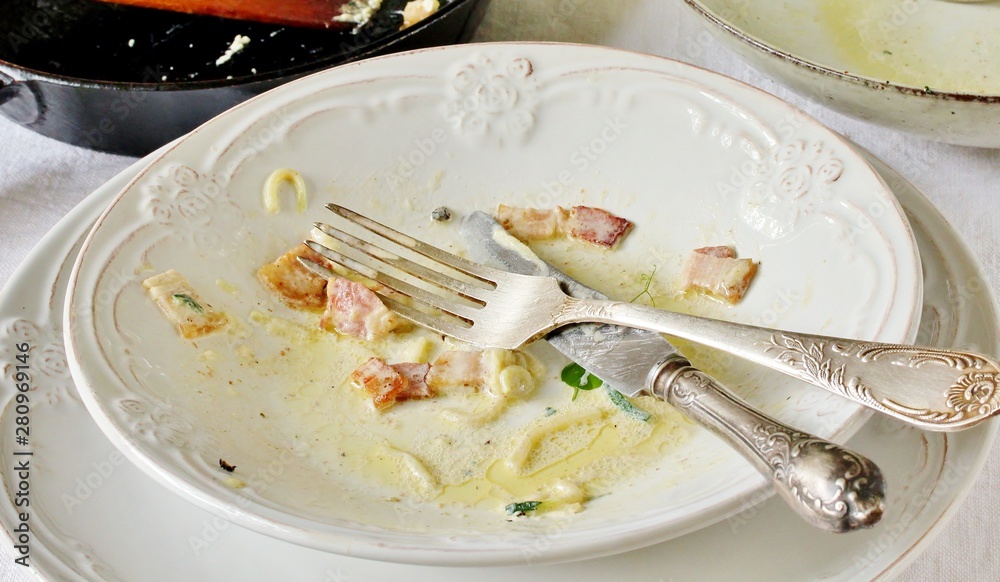 dirty dishes after eating pasta carbonara. bacon sauce in a plate