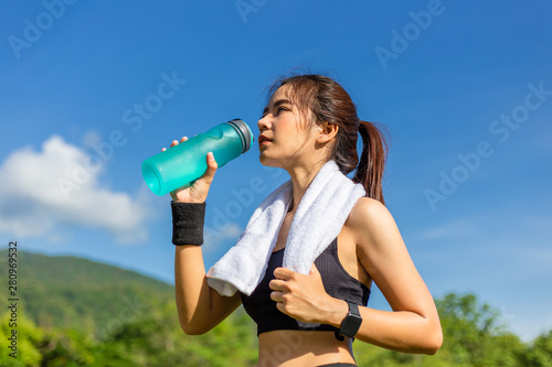 Beautiful young Asian woman exercising in the morning at a running track, taking a rest to drink water
