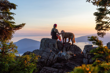 Adventurous Girl is hiking with a dog on top of St. Mark's Mountain during a sunny summer sunset. Located in West Vancouver, British Columbia, Canada.