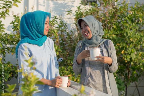 portrait of two hijab women drinking tea in front of the house and talking