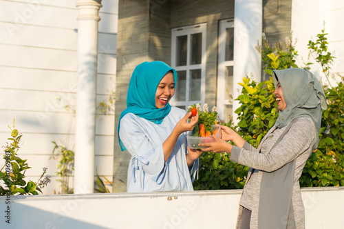 portrait of two hijab women sharing vegetables with neighbors in front of their house