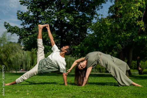 guy and girl masters different racial affiliation hold joint practice yoga in city park. lovely sunny weather. Tolerance, respect, calm, peace in world. Different asanas.