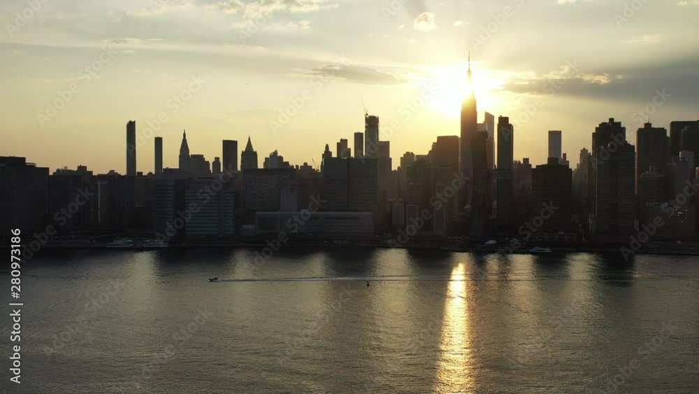 aerial drone camera pans left as a boat floats by in the same direction with a golden sunset & New York City in the background aerial drone camera pans left as a boat floats by in the same direction with a golden sunset & New York City in the background