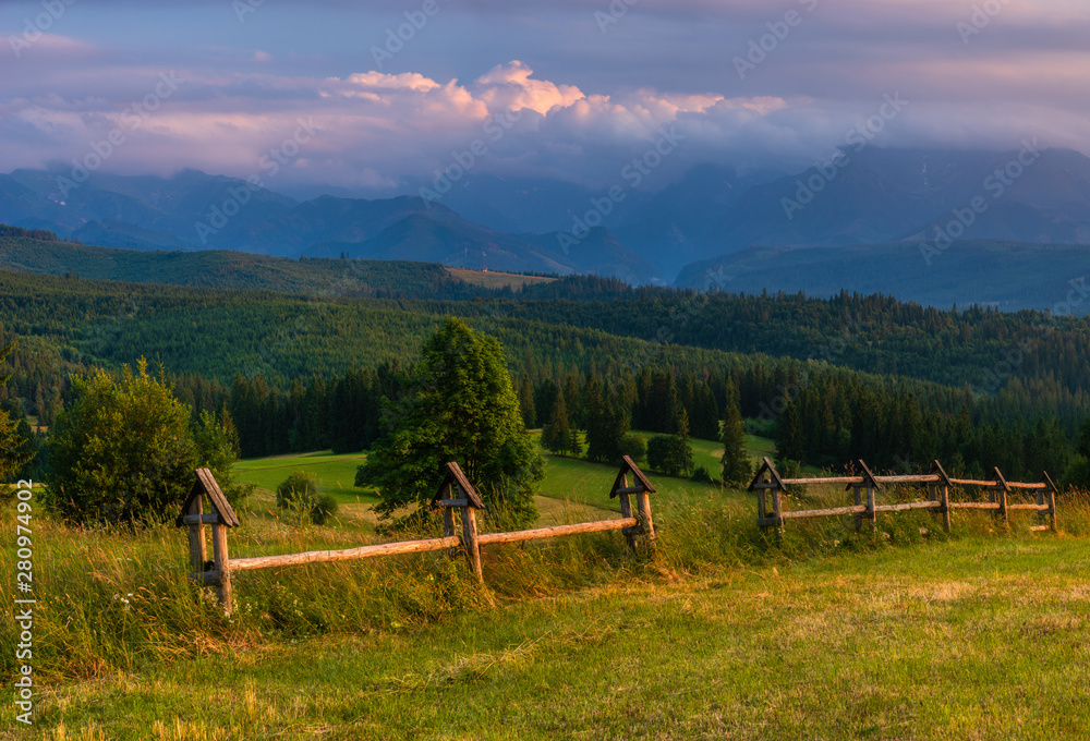  Tatra Mountains. Mountain peaks towering over green grassy hills. Above the peaks, beautiful storm clouds illuminated by the setting sun