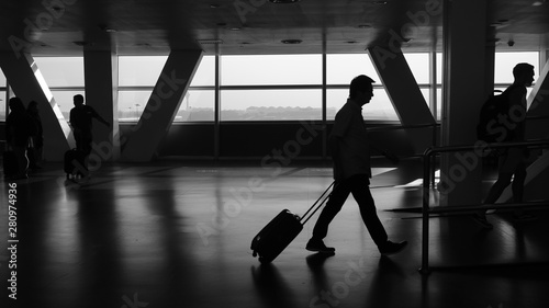 Silhouette of businessman pulling suitcase through airport on work/business trip