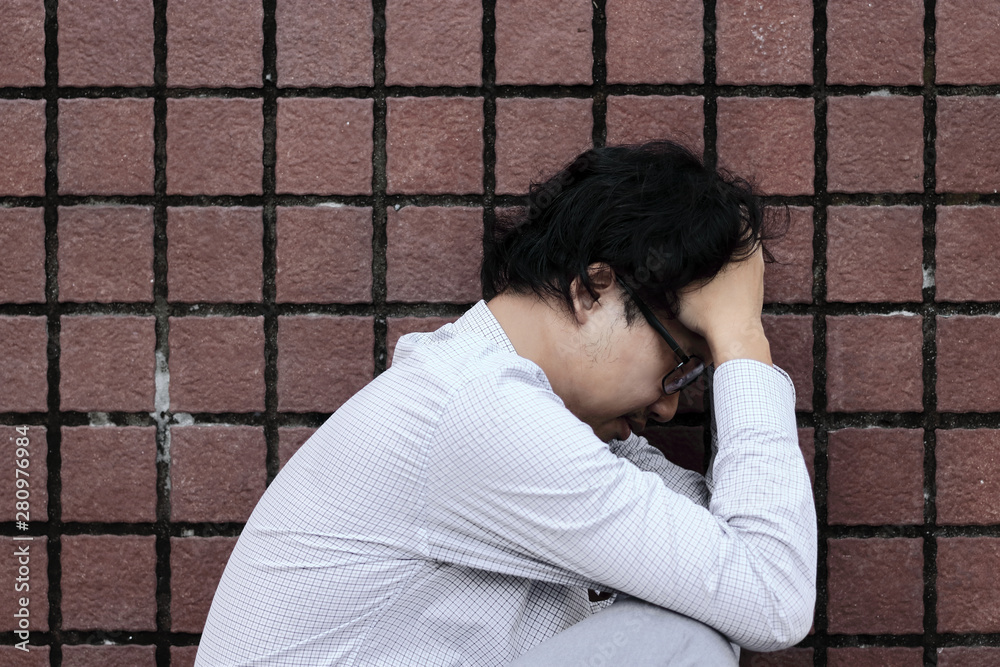 Side view of unhappy depressed young Asian man sitting and feeling bad Side view of unhappy depressed young Asian man sitting and feeling bad