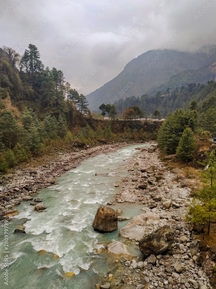 Dudh Koshi snow river (Dudh Kosi river or Milk-Koshi River) flows in mountain valley near Phakding village in Himalayas in Nepal. Nature, Lakes and Rivers, Mountains, Travel and Tourism concept. - obrazy, fototapety, plakaty 