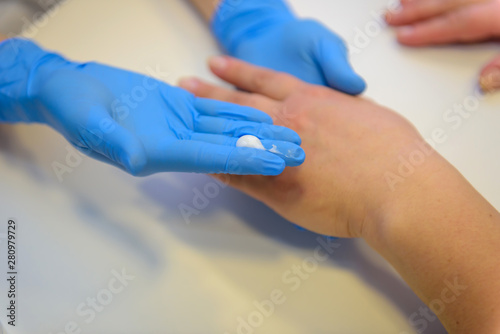 Beautician or manicurist in special medical gloves causes the cream on the woman s hand at the table in the Spa  close-up. Hand massage at the medical center. Professional care for hands.