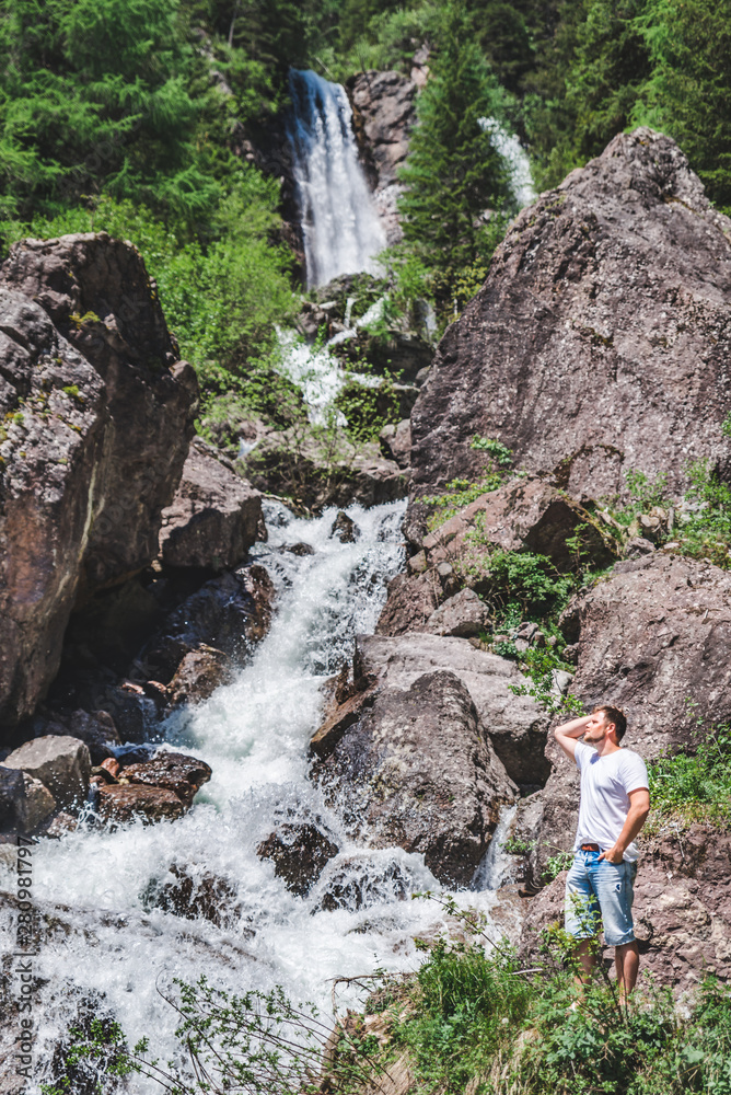 man in front of waterfall in mountains forest