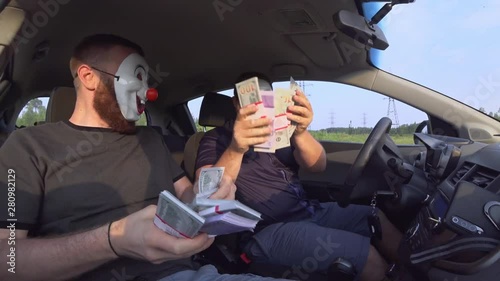 Two men in funny masks with guns in the car rejoice at money after a robbery. Armed robbers used weapons to rob money.