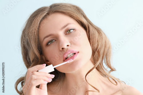 Beautiful young woman applying lipstick against color background