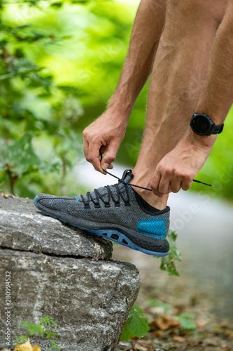 Running shoes sports smartwatch man tying shoe laces. Male fitness runner getting ready to jog in spring autumn jogging outdoor wearing technology wearable smart watch.