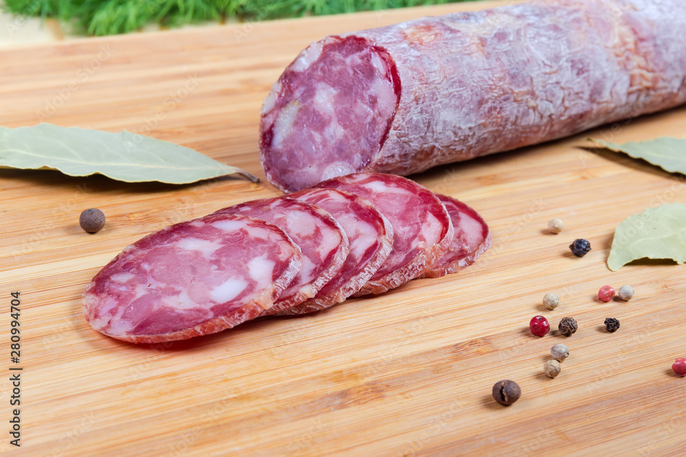 Partly sliced dry-cured sausage among spices on cutting board Partly sliced dry-cured sausage among spices on cutting board
