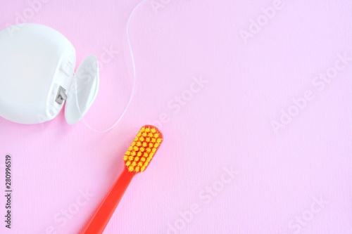 Red plastic toothbrush with yellow bristles and dental floss with selective focus on pink background with empty space for image or text. Toothbrush and hygienic dental thread for personal dental care
