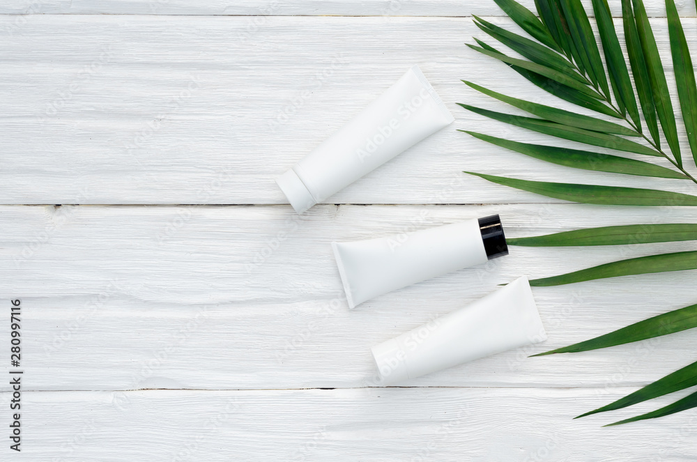 Body skin cream in a tube and a green leaf on a white wooden table background with copy space. Body skin cream in a tube and a green leaf on a white wooden table background with copy space.