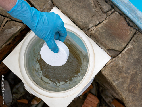 Female hand puts white tablets into pool skimmer. Cleaning, disinfection of water in the swimming pool. photo