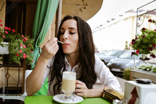 beautiful woman sits in a restaurant and eats latte from a spoon