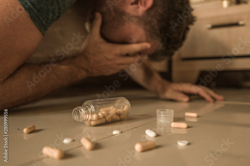 intoxicated man suffering depression crying on bed floor at home after having pills overdose intoxicated by mix of antidepressant medicines regret on suicide attempt photo
