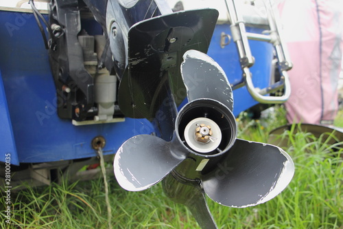 Close up lower unit of boat transom outboard motor - 3 blades propeller gear, bracket clamp with trim and tilt cylinder on blue boat transom and green grass background photo