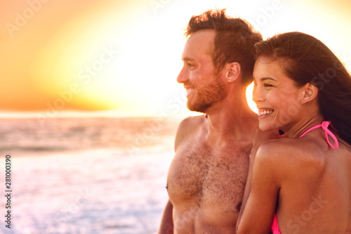 Sexy swimwear models relaxing on sunset beach summer vacation. Healthy young couple smiling living holiday surfers lifestyle. Asian girl, Caucasian man in their 20s, with tanned body. © Maridav