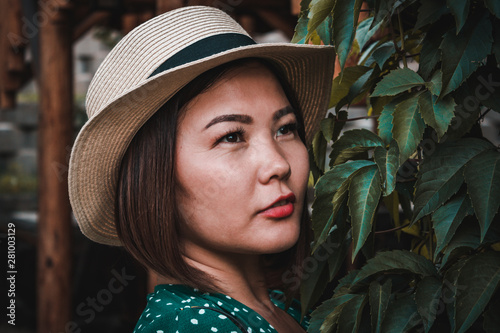 Beautiful Asian stands near the bush and looks into the distance.
