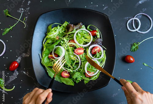 Eat green concept with organic fresh vegetable salad in ceramic plate on black background.