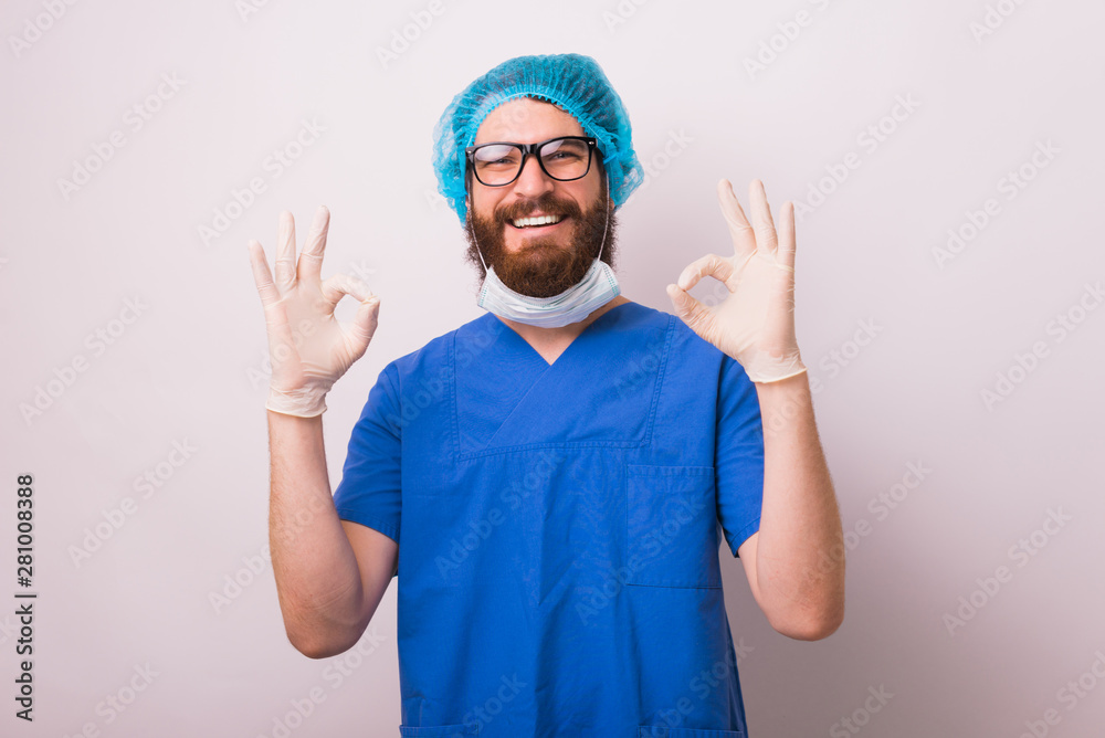 Portrait of smiling cheerful doctor man showing OK sign gesture over white wall Portrait of smiling cheerful doctor man showing OK sign gesture over white wall