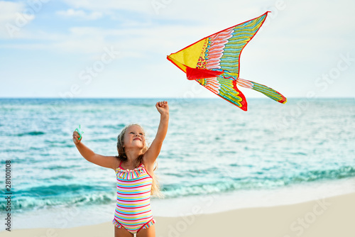 Happy little girl with flying kite on tropical beach