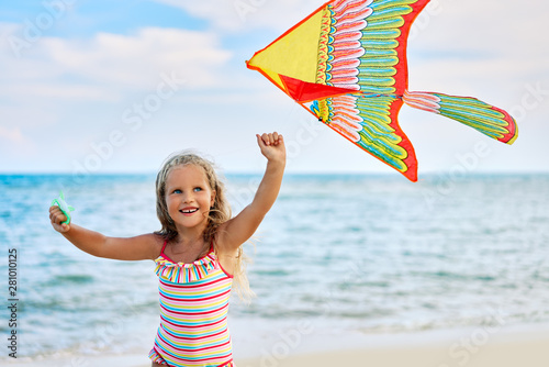 Happy little girl with flying kite on tropical beach