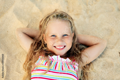 Pretty little blonde girl portrait lying on sandy beach during summer vacation