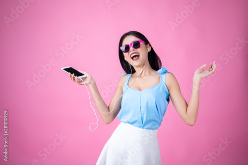 Young asian woman in headphones listening to music and dancing on pink background 