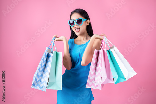 Portrait of a happy Asian pretty girl holding shopping blue bags away isolated over pink background,colorful shopping concept.