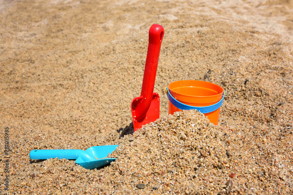 Bright plastic сhildren's beach toys - bucket and shovels on sand near sea Bright plastic сhildren's beach toys - bucket and shovels on sand near sea