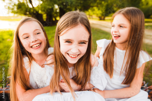 Three girls in white dresses walk in nature in the summer. Children's pastime during the summer holidays.