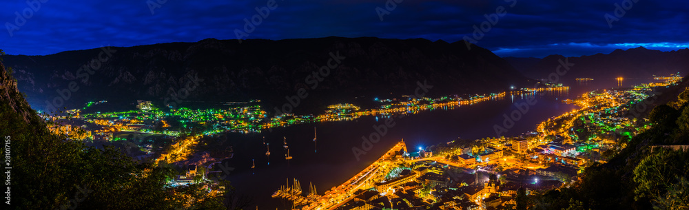 Montenegro, XXL panorama of illuminated houses, streets, harbor and old town of city of kotor bay at night from above surrounded by majestic mountains and waterside
