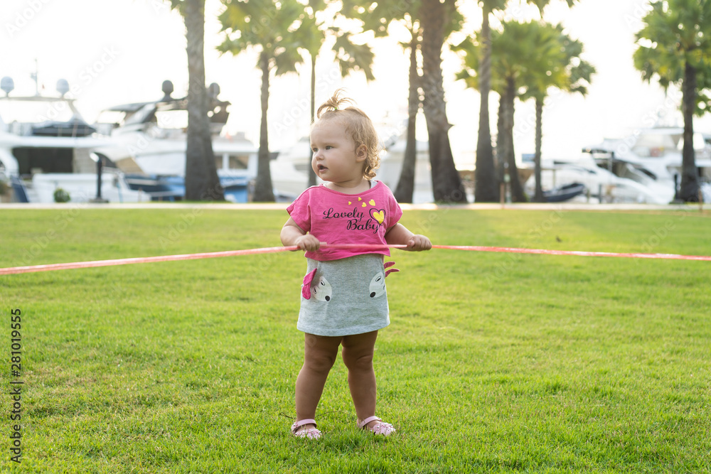 A little girl of 1 year old running on a green meadow in a park among palm trees and cutting a red ribbon A little girl of 1 year old running on a green meadow in a park among palm trees and cutting a red ribbon