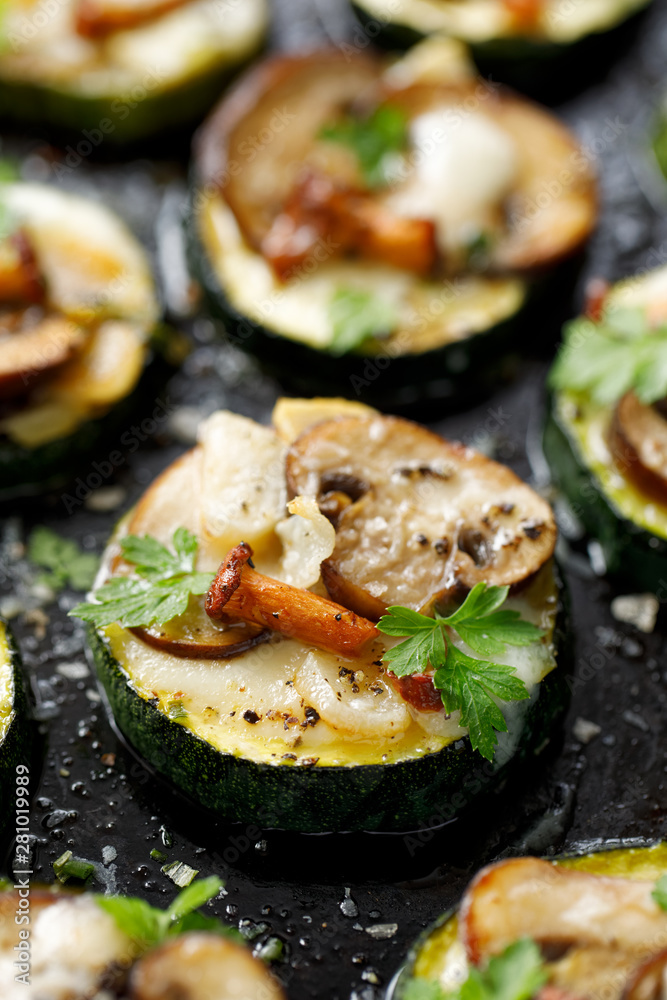 Zucchini pizza bites from zucchini slices with the addition of brown mushrooms, chanterelles, mozzarella cheese and herbs on a black background, top view, close-up. Vegetarian food Zucchini pizza bites from zucchini slices with the addition of brown mushrooms, chanterelles, mozzarella cheese and herbs on a black background, top view, close-up. Vegetarian food