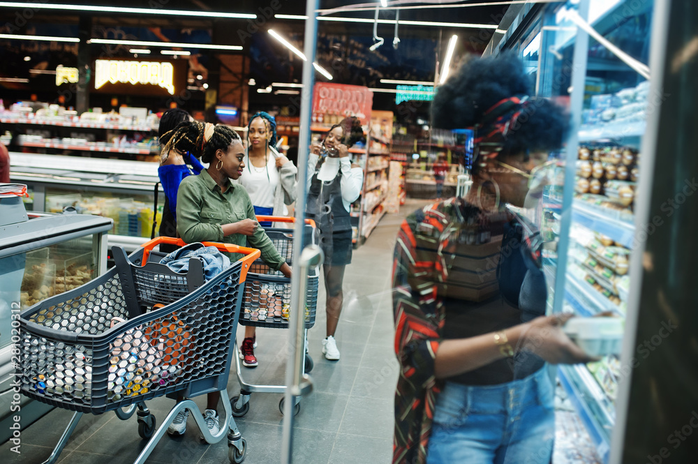 Group of african womans with shopping carts near refrigerator shelf selling dairy products egg carton in the supermarket.